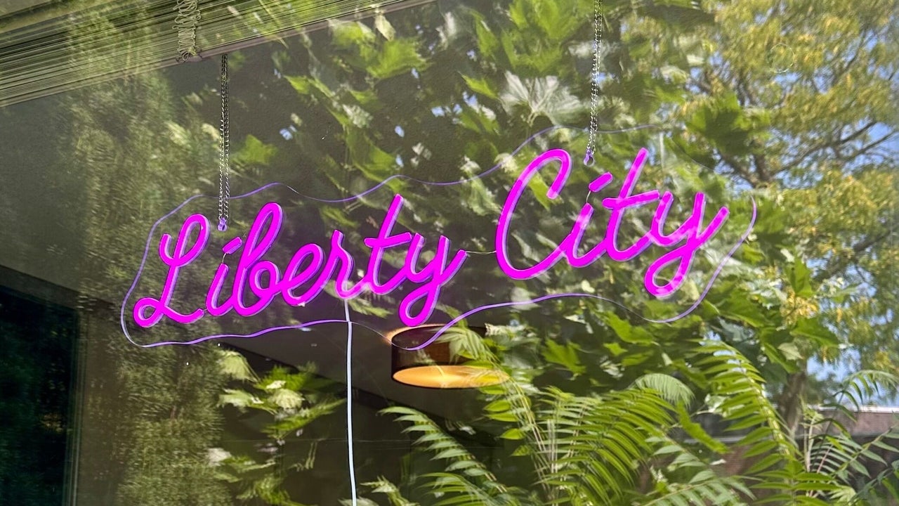 Het roze neonbord Liberty City in het raam van de studio, met varens erachter