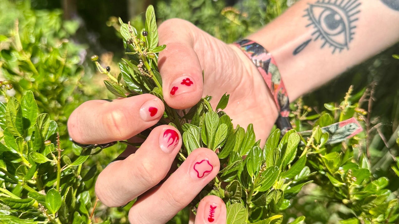 Korte naturel nagels met rode nail art, een hand tussen groene blaadjes