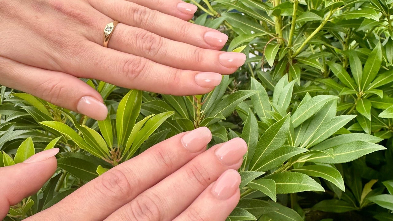 Twee handen met korte, natuurlijke nude nagels tussen groene bladeren